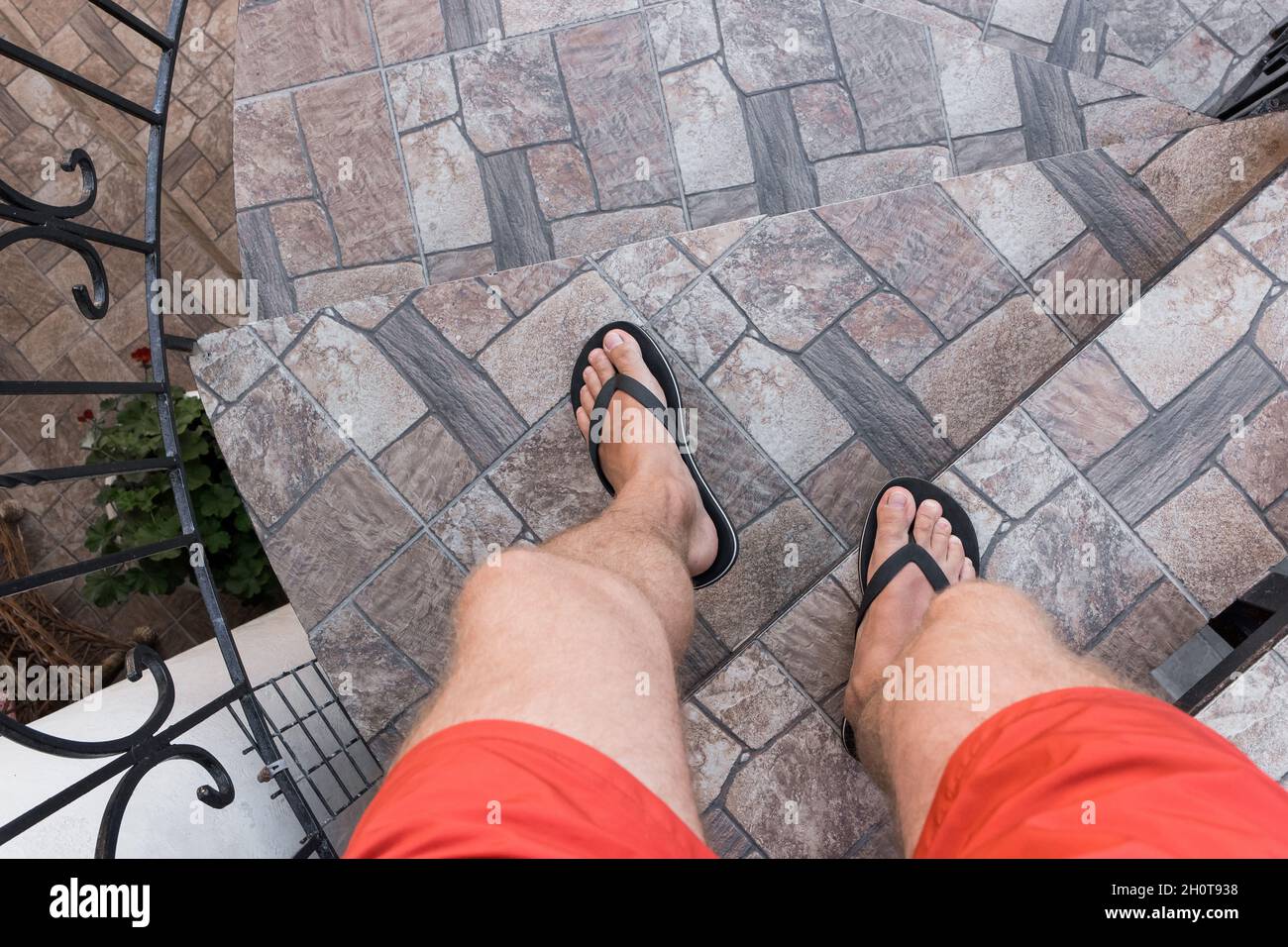 Men's legs in black flip flops and red shorts go down and walk down the stairs. Walking style. Stock Photo