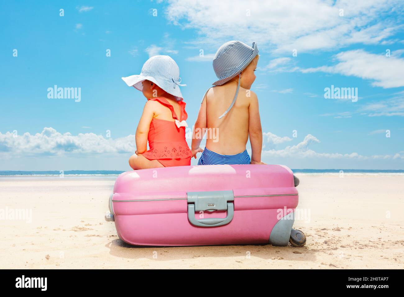 Two children sit on suitcase at the beach concept Stock Photo