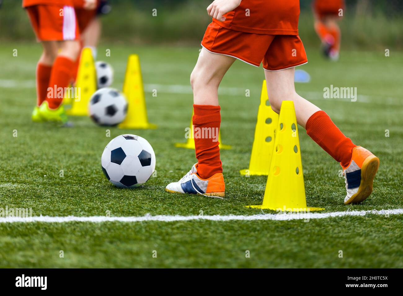 Closeup image of football players running balls between training cones on practice unit. Young boys on football camp. School soccer players improving Stock Photo