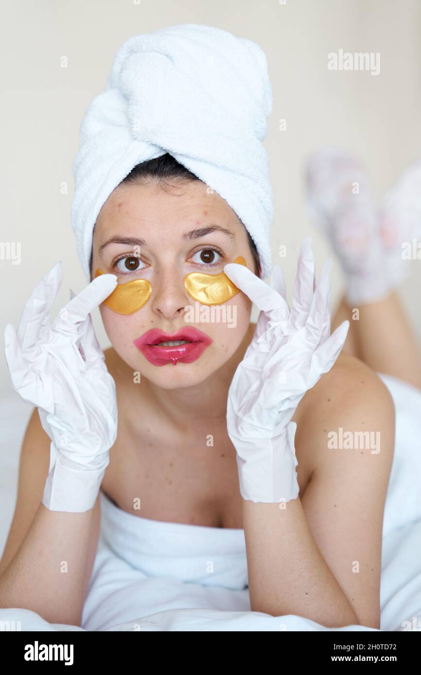 After a shower, a girl wrapped in a towel uses cosmetic patches for the