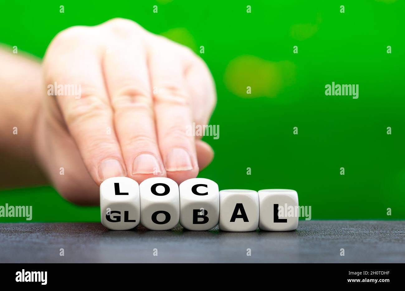 Hand turns dice and changes the word global to local. Stock Photo
