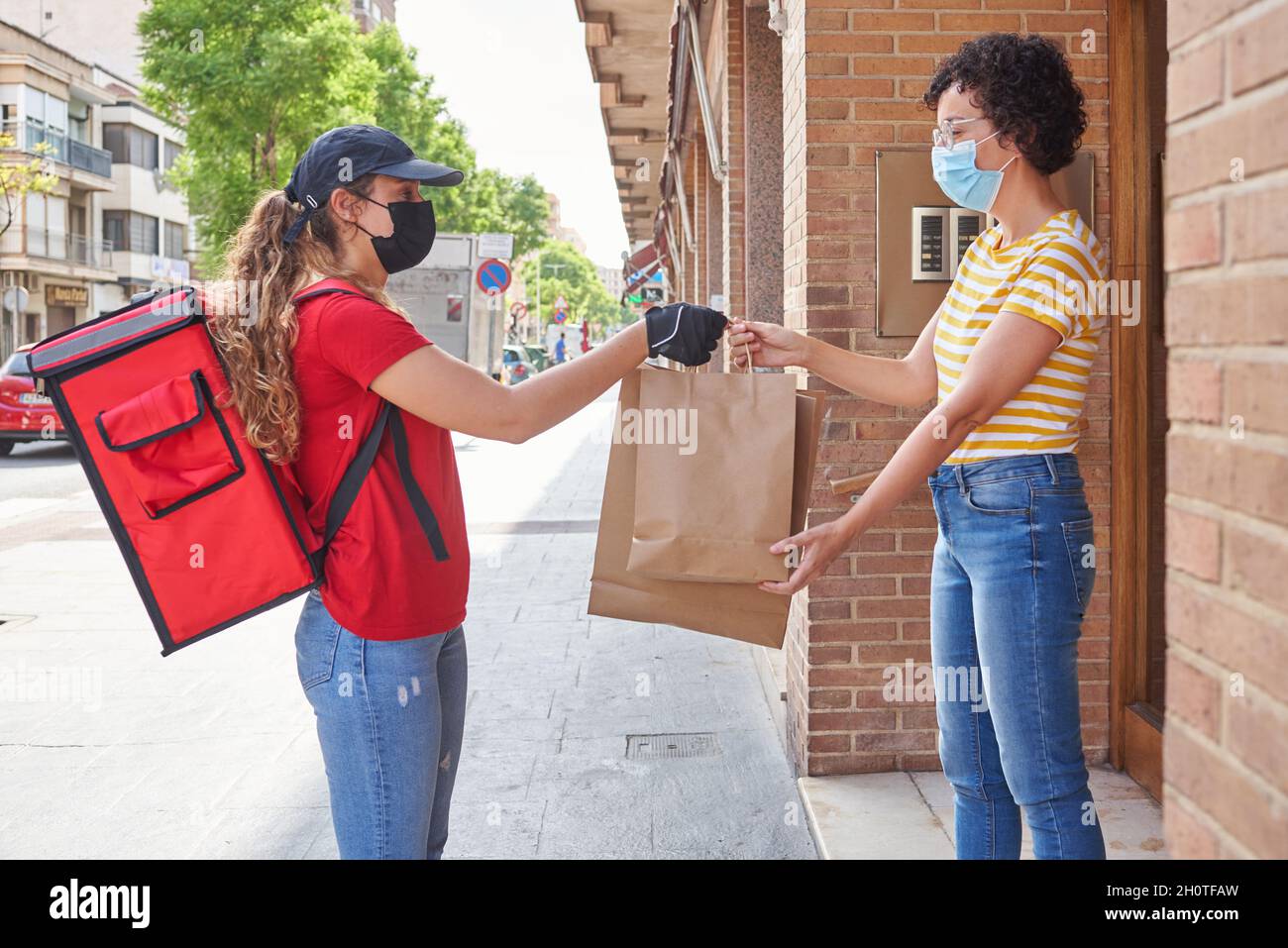 A delivery girl with a face mask delivers bags of food on the street Stock Photo