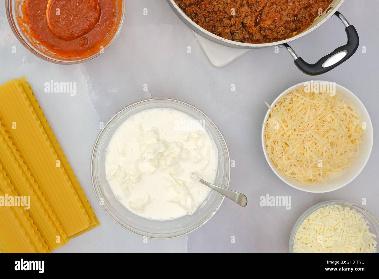 Raw lasagna noodles, ground beef on frying pan, marinara, and cheese in