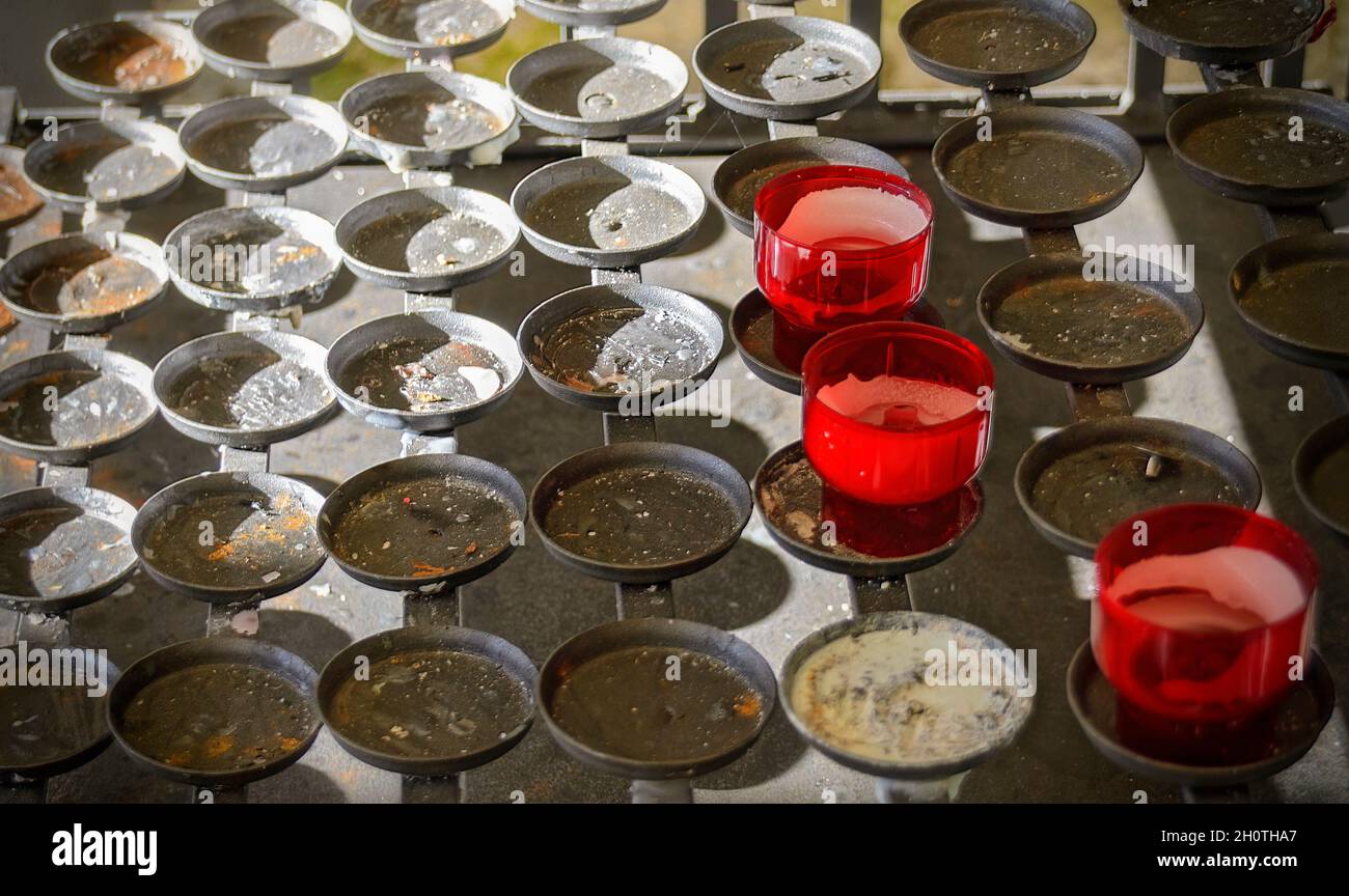 metallic stand with empty flat candleholders for votive candles and remnants of burnt down red candles Stock Photo