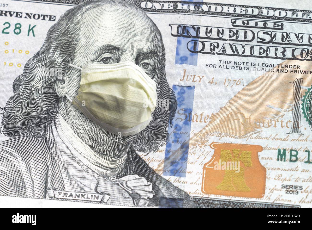 Close up of United States paper currency one hundred dollar bill with Benjamin Franklin wearing yellow doctor mask due to COVID-19 pandemic making a g Stock Photo