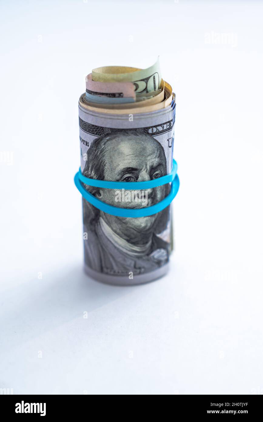 Close up of a rolled up wad of cash sitting on edge with a blue rubber band wrapping across Benjamin Franklin's face on a hundred dollar bill Stock Photo