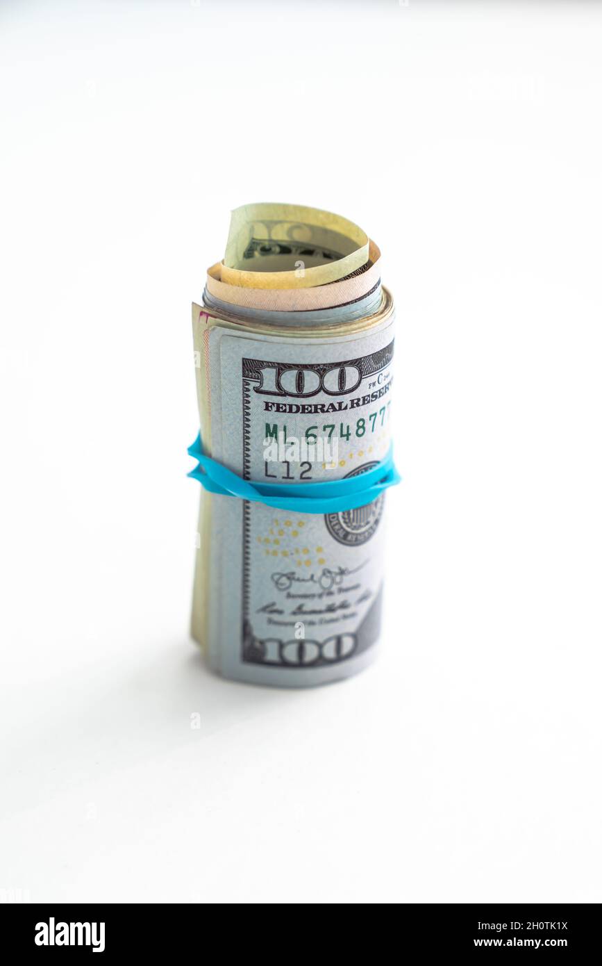 Close up of a rolled up wad of cash on edge with a blue rubber band wrapped around with hundred dollar bill on top isolated on a white background Stock Photo