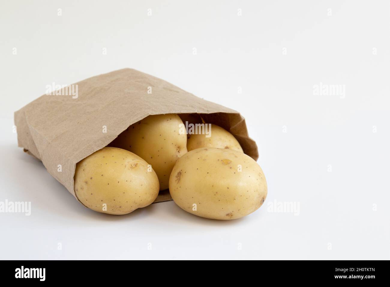 pile of fresh raw potatoes in small paper bag isolated on white