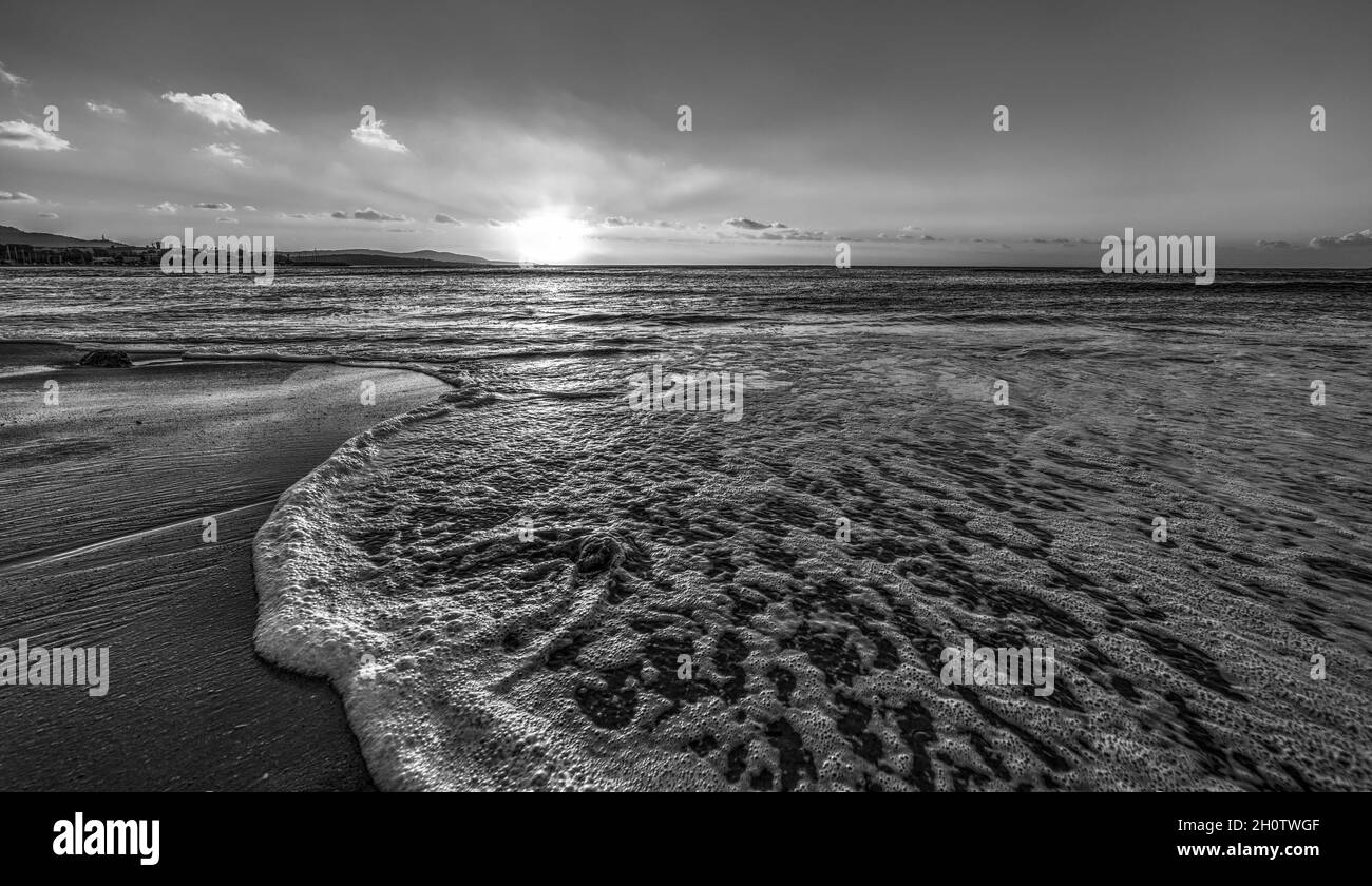 Sea foam in Alghero shore at sunset. Sardinia, Italy. Black and white effect Stock Photo