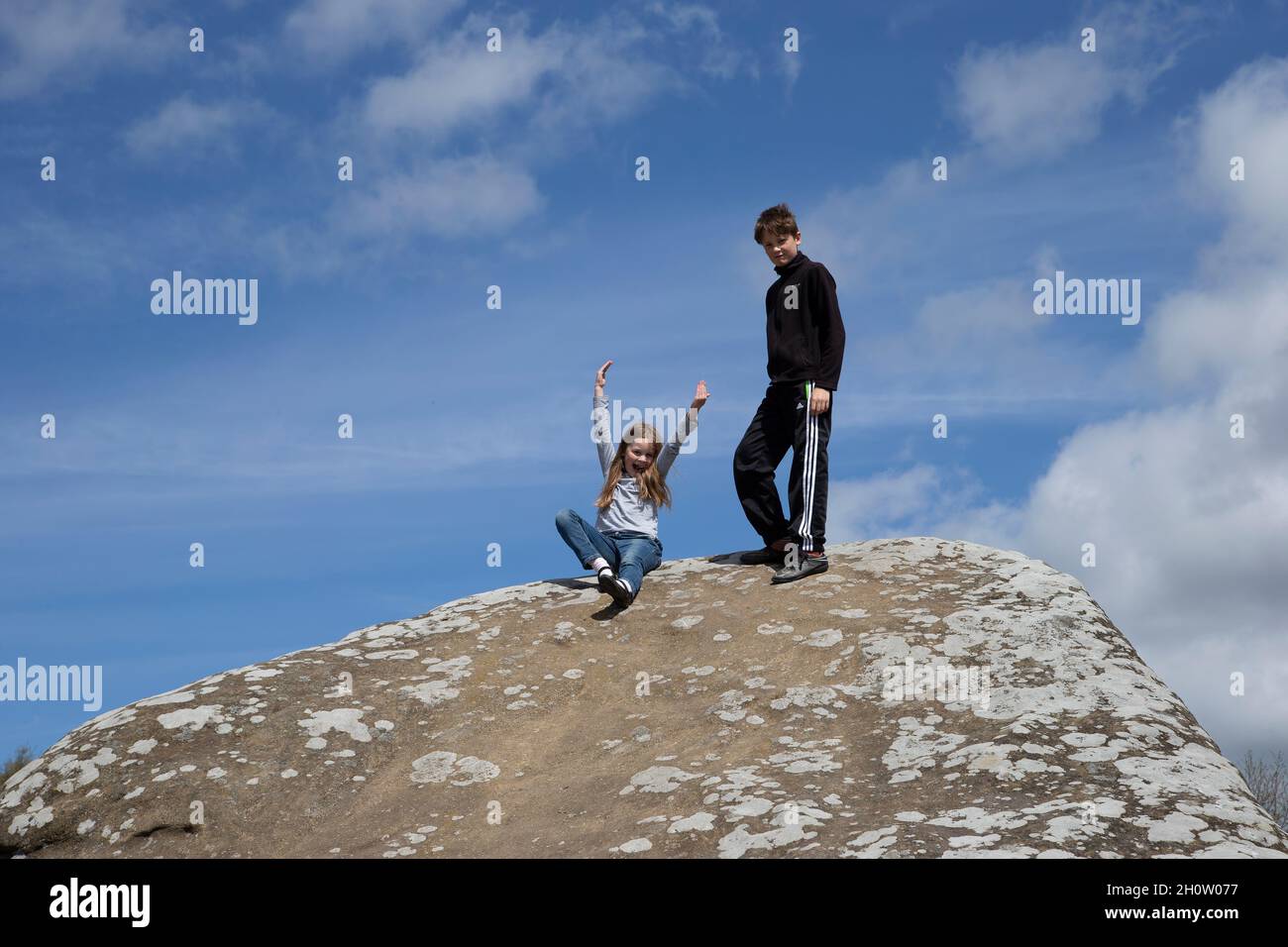 Young boy and girl enjoying themselves having climbed to the top of a large rock against a blue summer sky in northern England U.K. Stock Photo