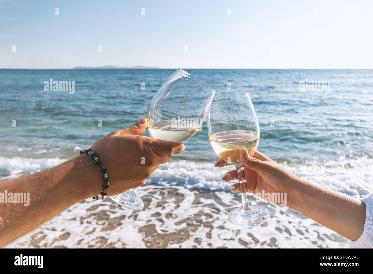 Two hands with glasses of wine on the beach. Summer vacations concept