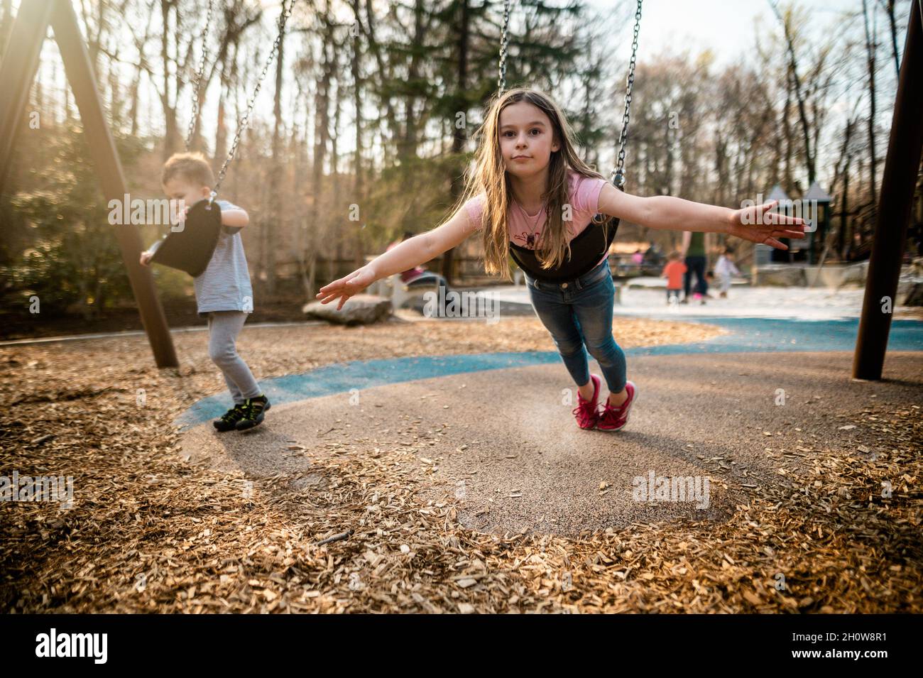 Brother and sister play on the swings at playground at sunset Stock ...