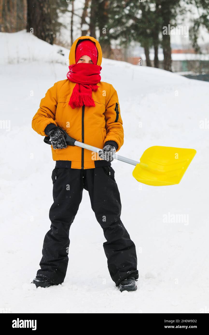 boy in yellow jacket and red hat with scarf with shovel in his hands on a snowy street. Stock Photo