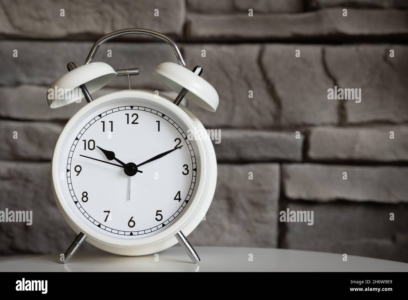 small white retro alarm clock with a grey stone background and copy