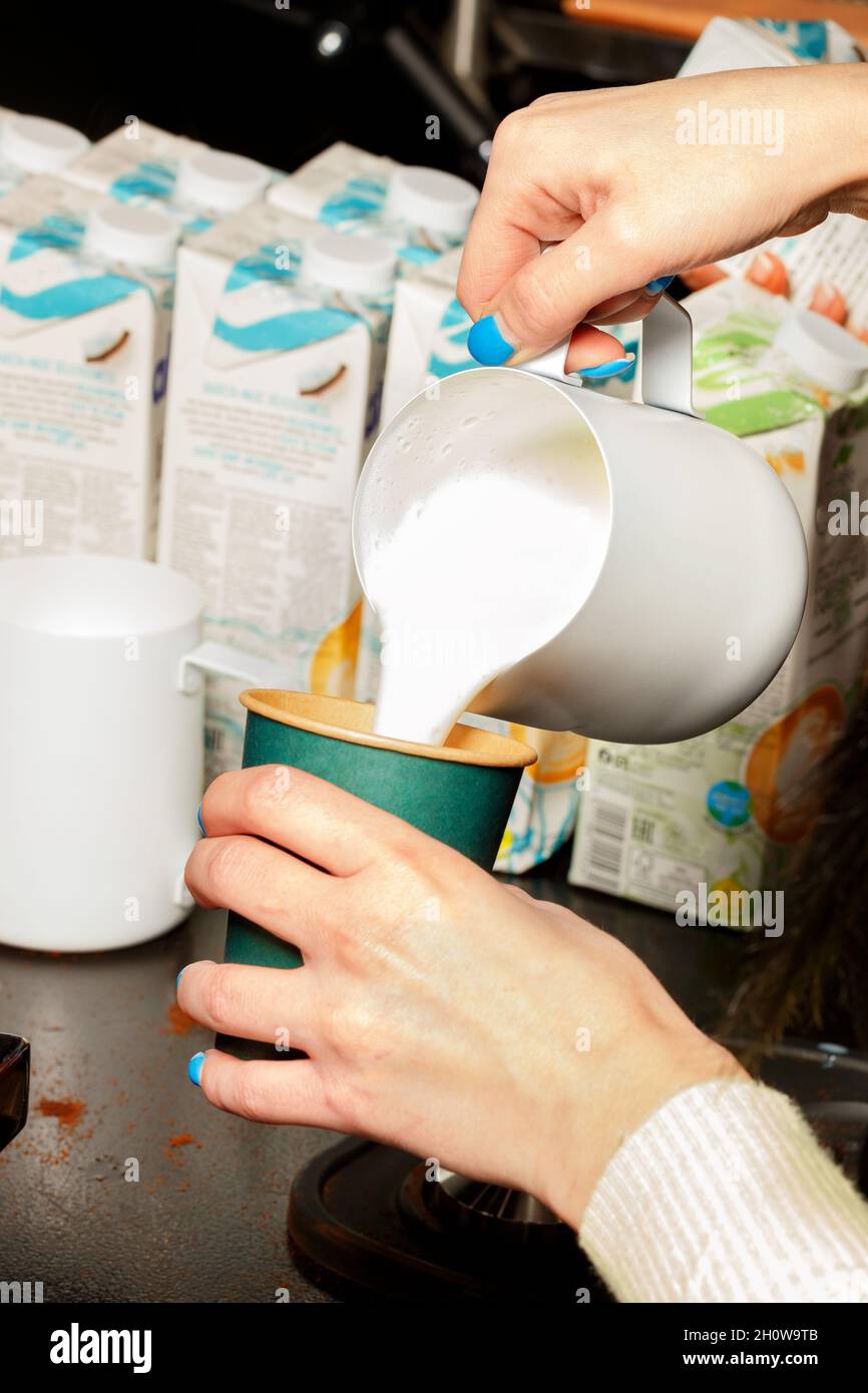Close-up shot of a barista adding frothed milk to coffee in a paper ...