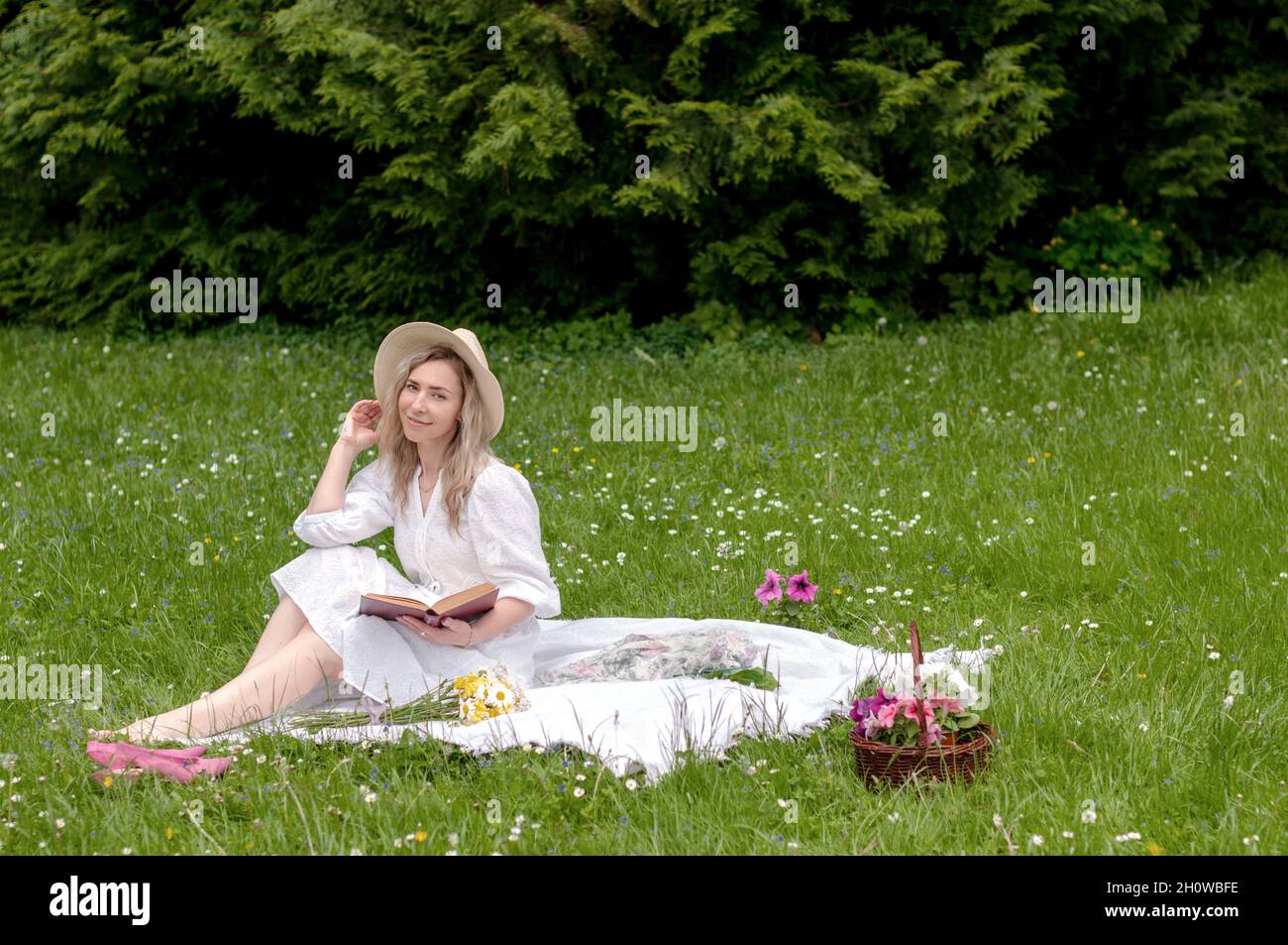 A smiling girl with a book on a blanket in the forest. Stock Photo