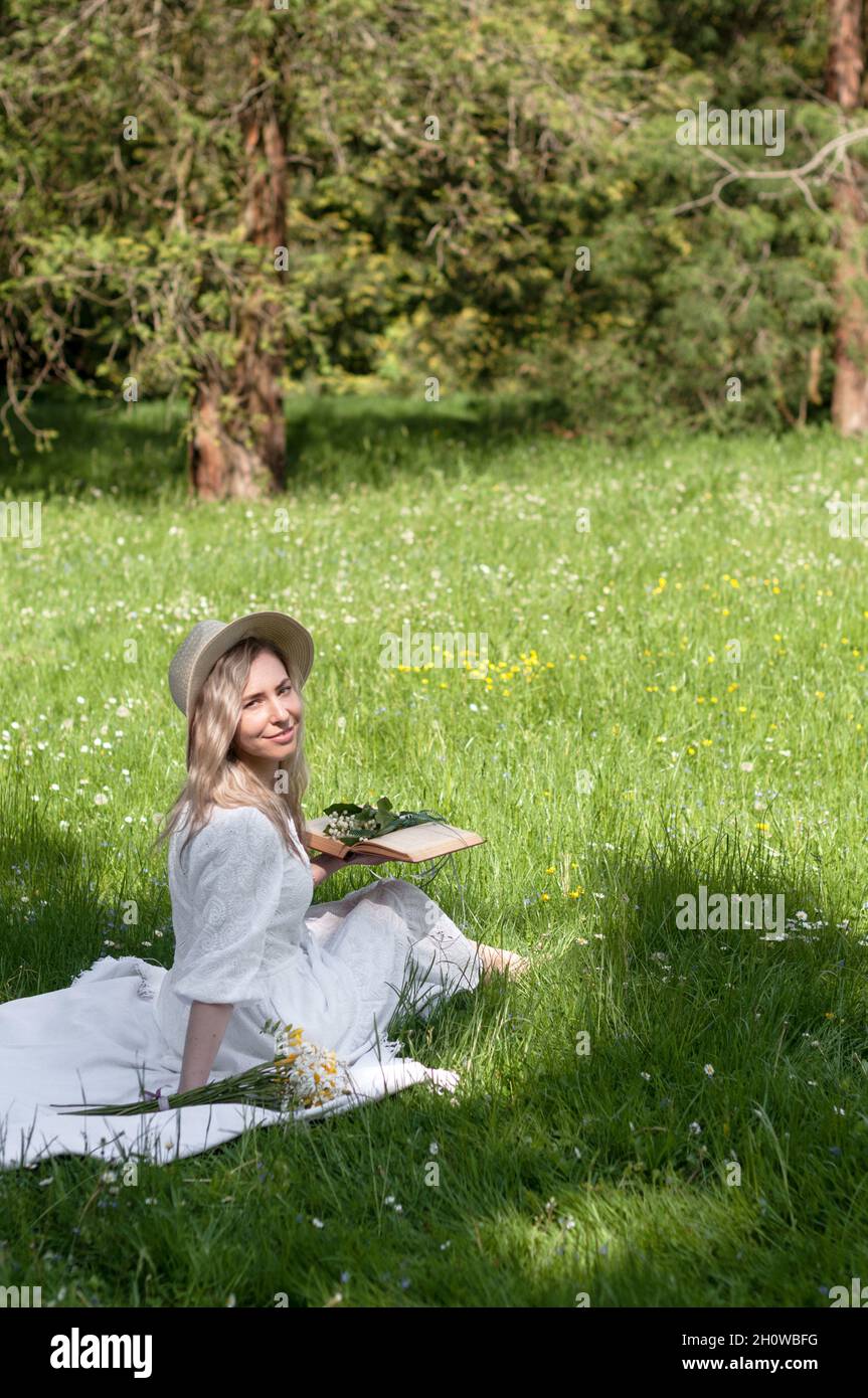 Girl in a hat with a book, sitting on a blanket in sunshine. Stock Photo