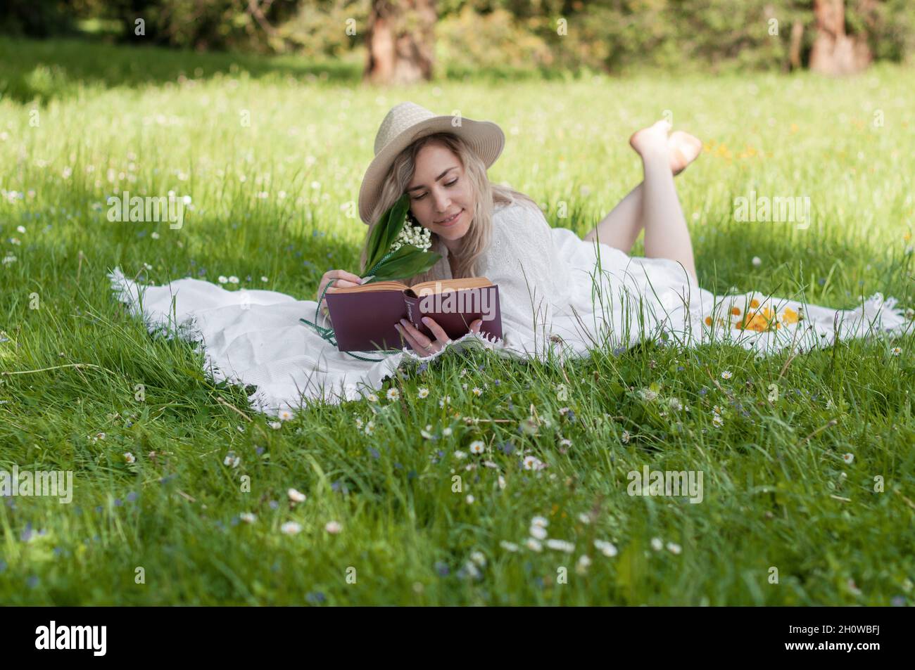 Girl in a hat with a book, lying on a blanket. Stock Photo