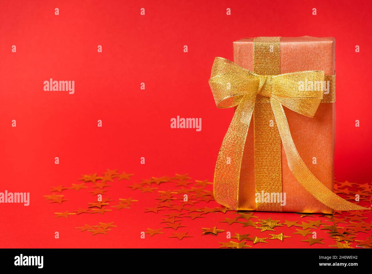 Gift box in a gold wrapper with a gold bow on a starry colored ...