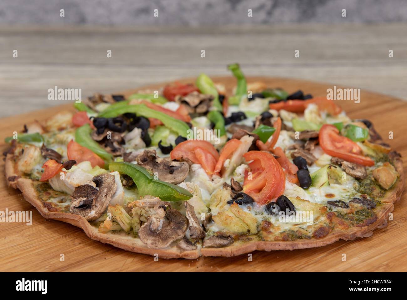 Freshly baked cauliflower crust pizza with chopped vegetable toppings served on a wooden platter. Stock Photo