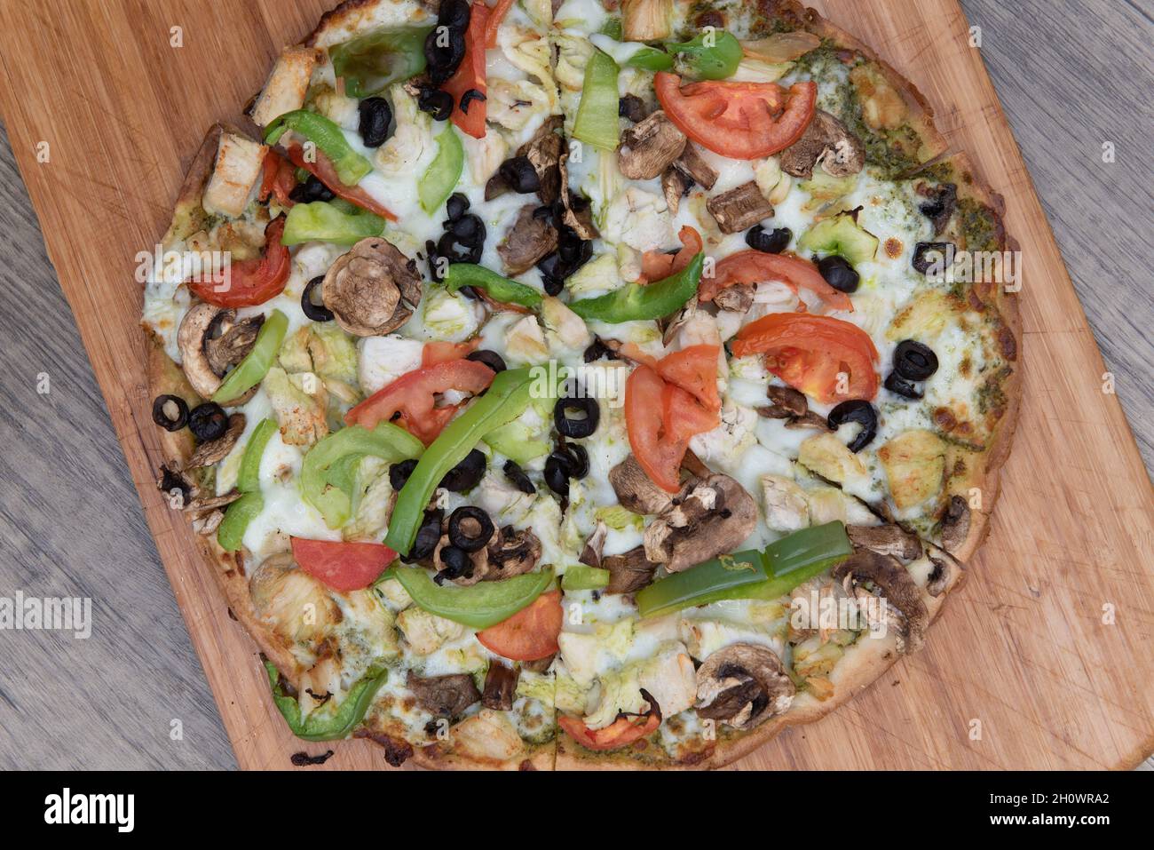 Overhead view of freshly baked cauliflower crust pizza with chopped vegetable toppings served on a wooden platter. Stock Photo