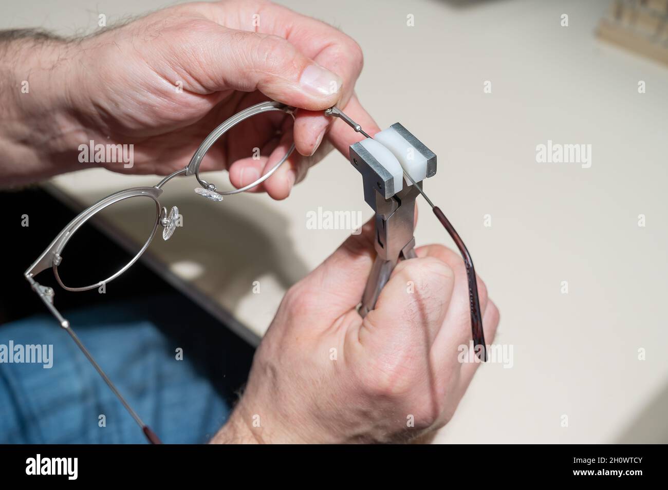 The man bends the temples of his glasses. The master repairs the frame with tongs. Stock Photo