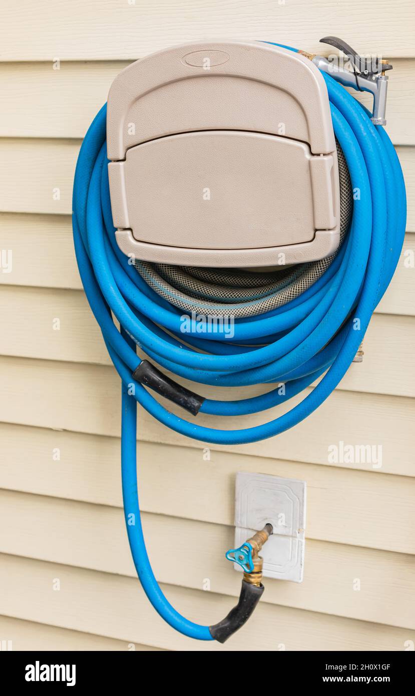 Blue gardening hose hanging on the house wall. Garden hose hangout, wall hose reel. Street photo, selective focus, concept photo equipment for gardeni Stock Photo