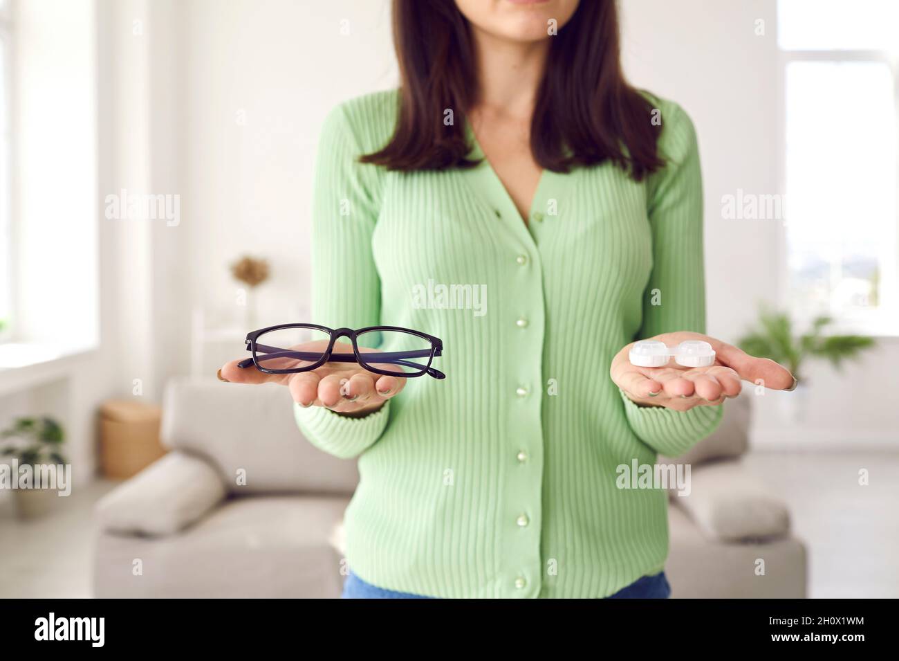 Young woman is holding glasses and eye lenses and trying to choose which to wear Stock Photo
