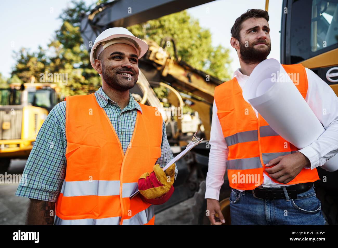 Two men engineers discussing their work standing against construction machines Stock Photo