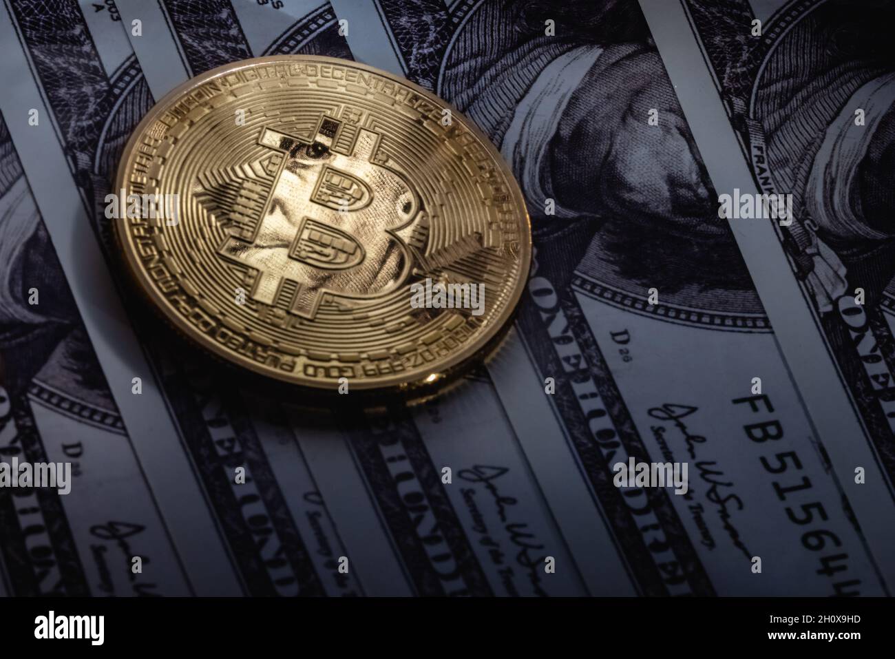 Gold bitcoin on one hundred dollar bills. The coin reflects the eyes of Benjamin Franklin. Stock Photo