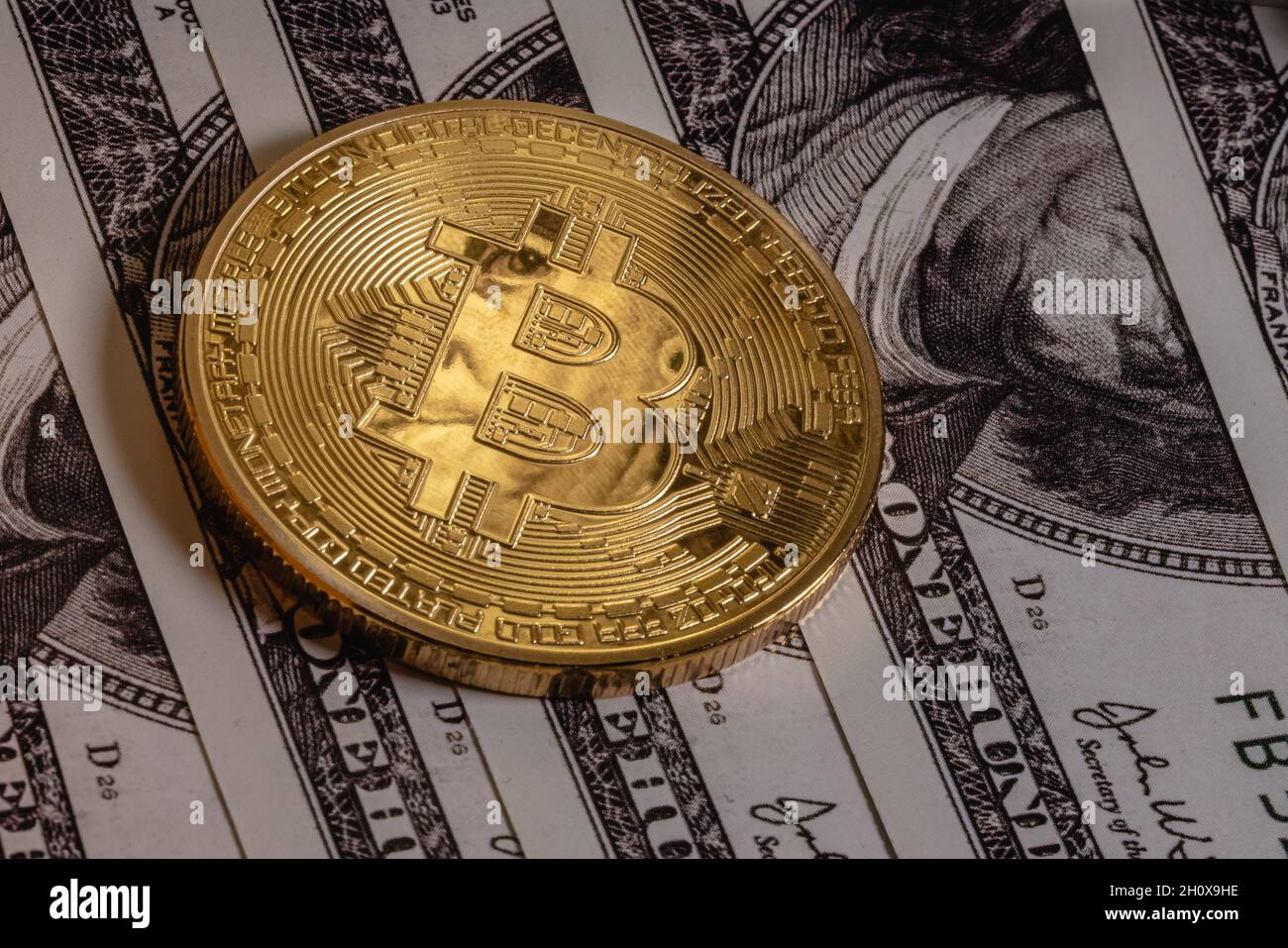 Gold bitcoin on one hundred dollar bills. The coin reflects the eyes of Benjamin Franklin. Stock Photo