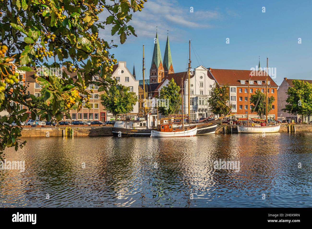 Lübeck, fishing and tourism boats moored on the river Trave.The two Gothic bell towers of the curch of Santa Maria. Lübeck, Germany Stock Photo