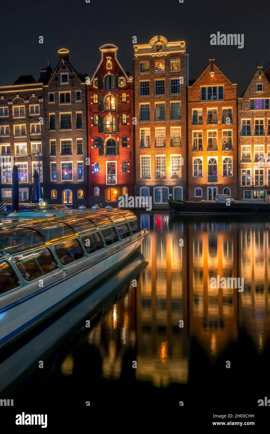 Netherlands. Night Amsterdam. Multi Colored windows of typical houses near the water and a pleasure boat Stock Photo