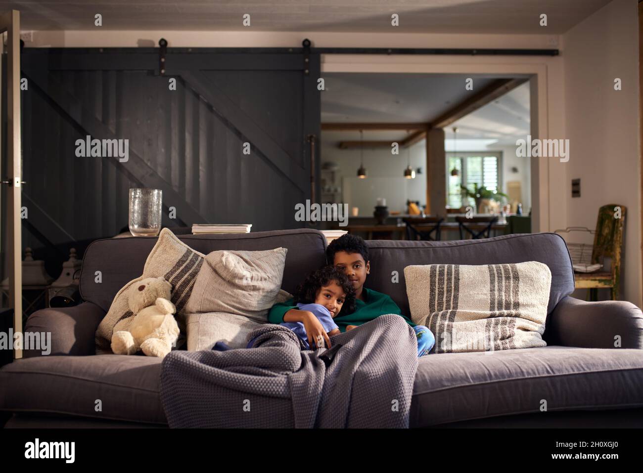 Two boys cuddling on sofa under blanket Stock Photo