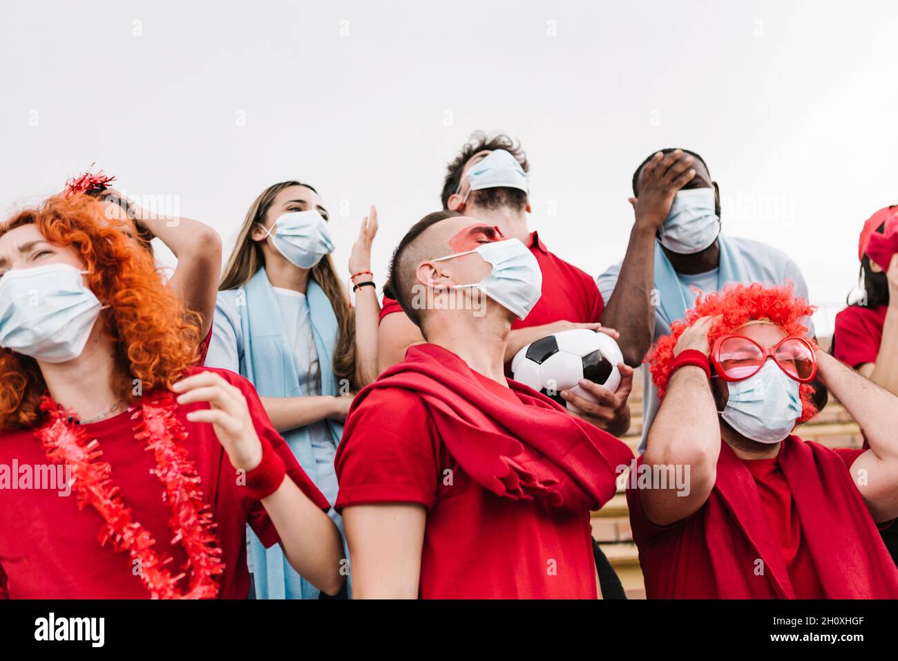 Frustrated group of multiracial soccer fans in protective face mask watching their football team losing - Focus on man in the center Stock Photo