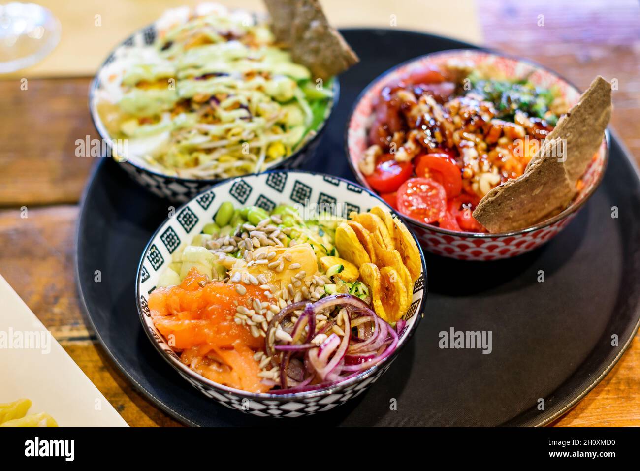 High angle of delicious poke bowls with different vegetables and beans with seeds and onion with fish placed on tray on wooden table in light restaura Stock Photo