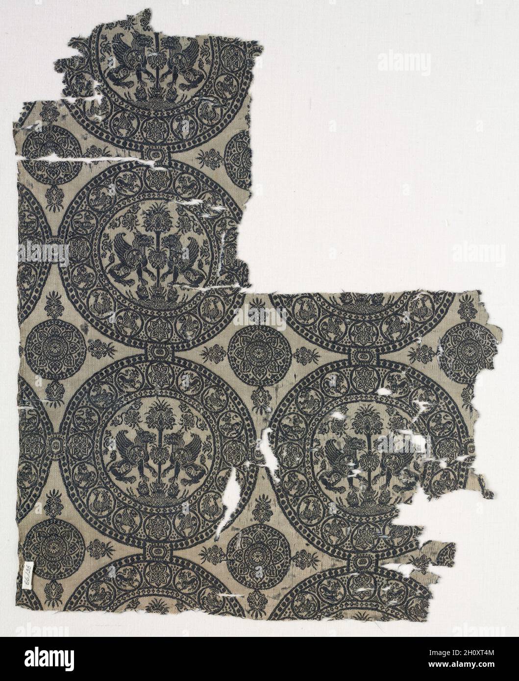 Fragments with Griffins in Roundels, before 1966. Iran or Iraq, in the style of the Seljuq period (1037–1194). Lampas weave, silk; average: 41 x 32.8 cm (16 1/8 x 12 15/16 in.).  This fragment consists of two almost complete roundels in lower right and fragment of third one at the left, plus parts of other roundels. In the roundels are a pair of confronted, winged griffins either side of a 'palm' tree. Heavy baroque floral motifs fill the spaces between the main motifs and the roundel frame. The palm grows out of a curious foliate device at the bottom. The roundel frame has pearl borders betwe Stock Photo