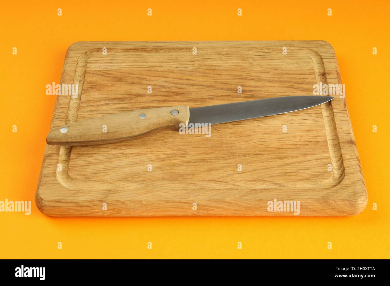 Cutting board with knife on orange background. Stock Photo