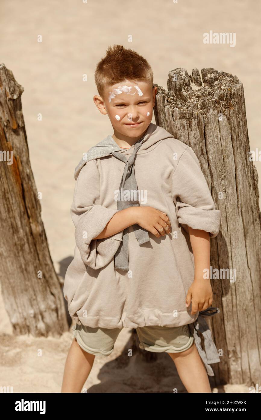 Boy in cozy beige clothes applying sunscreen protection creme on his face. Sun protection  during summer sea vacation. Children healthcare at travel t Stock Photo