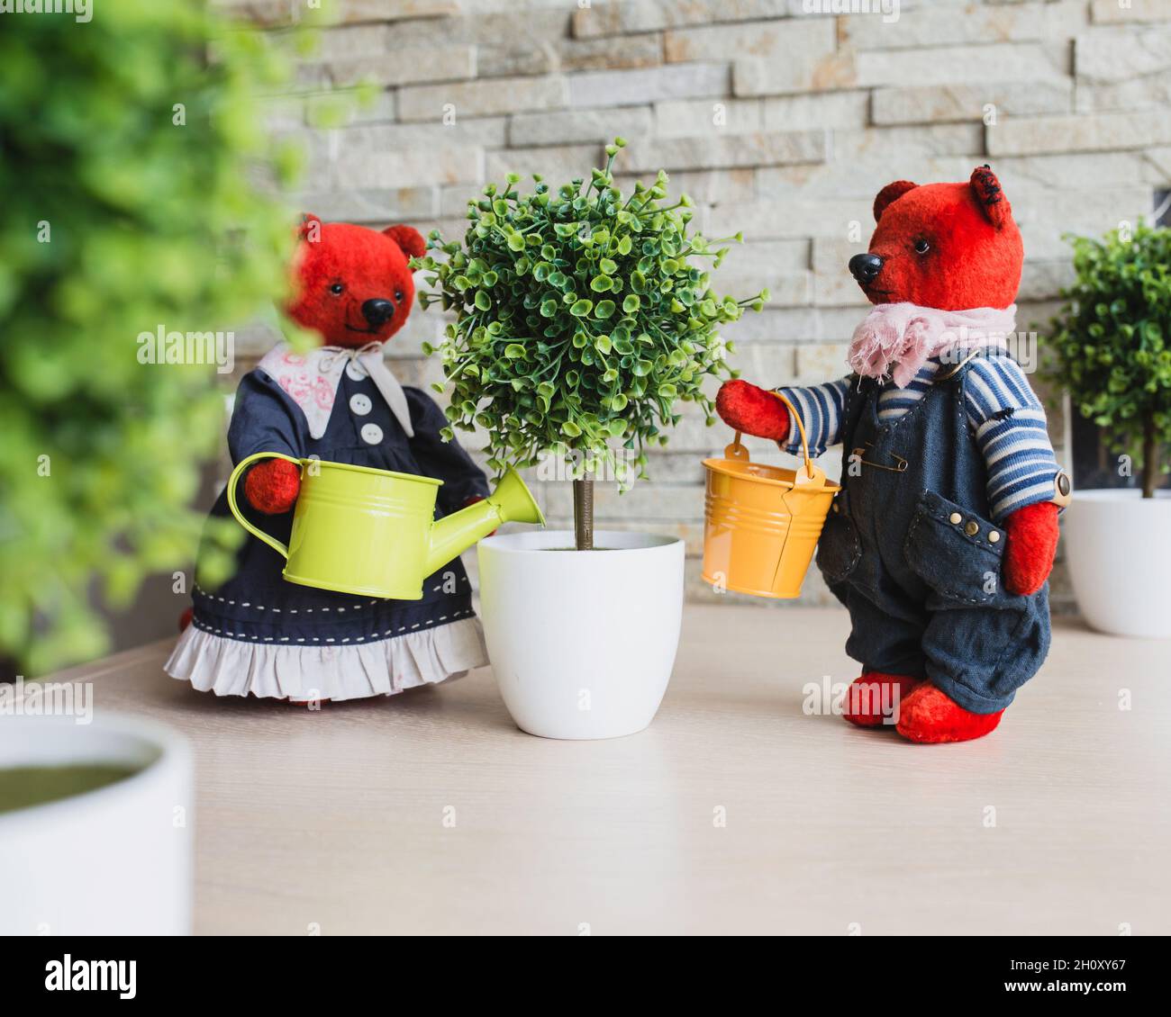 Installation of toys - plush handmade bears watering an artificial tree in the garden Stock Photo