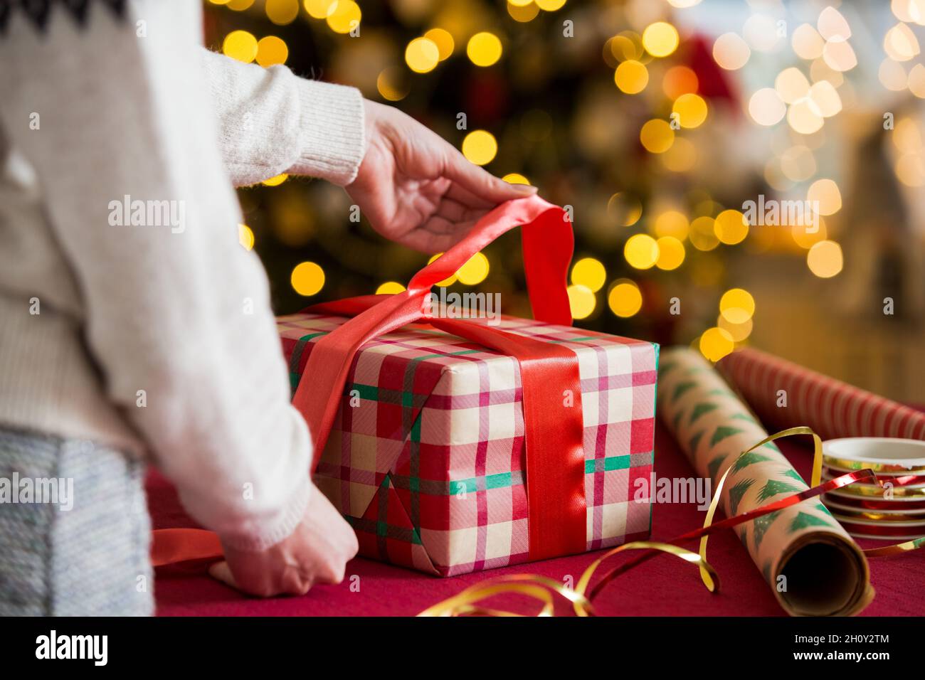 Man and woman preparing for Christmas. Couple in warm sweaters wrapping gifts. Decorated Christmas tree, boxes with presents, colourful wrapping paper Stock Photo