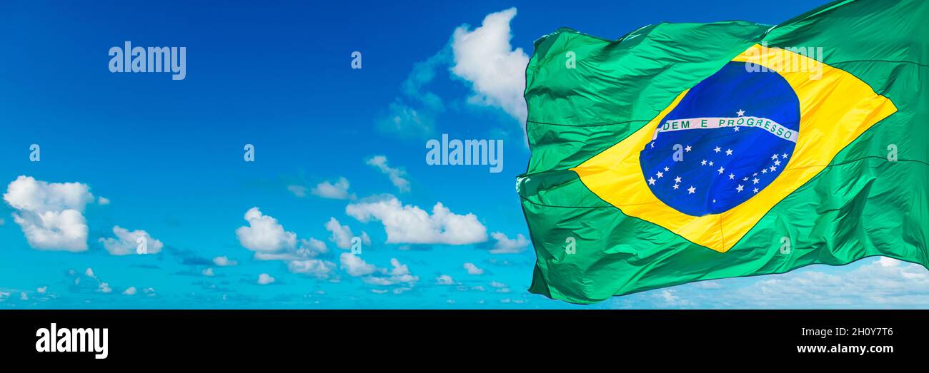Flag of Brazil waving in the wind against a blue sky with white clouds ...