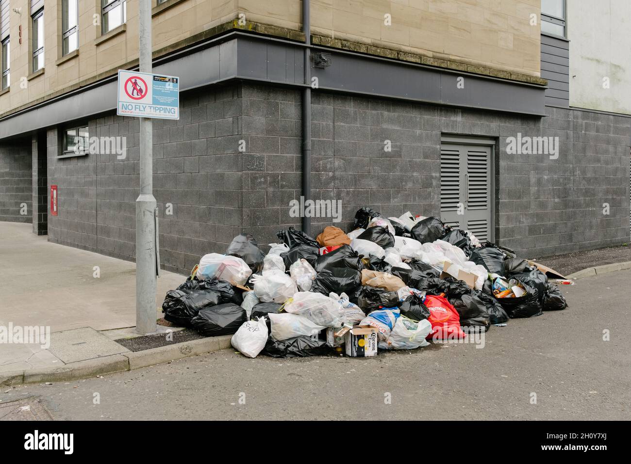 Lots of illegally dumped rubbish, or waste that has been flytipped in the city of Glasgow next to a sign that reads, No Flytipping. Stock Photo