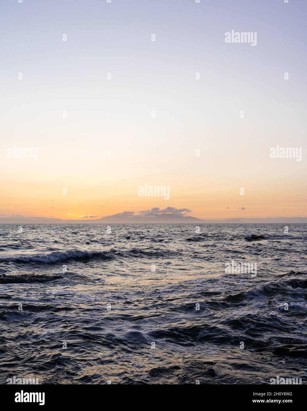 View at sunset of the Scottish Island of Arran across the sea from Troon at with the Goatfell mountain range on the horizon lit by the setting sun. Stock Photo