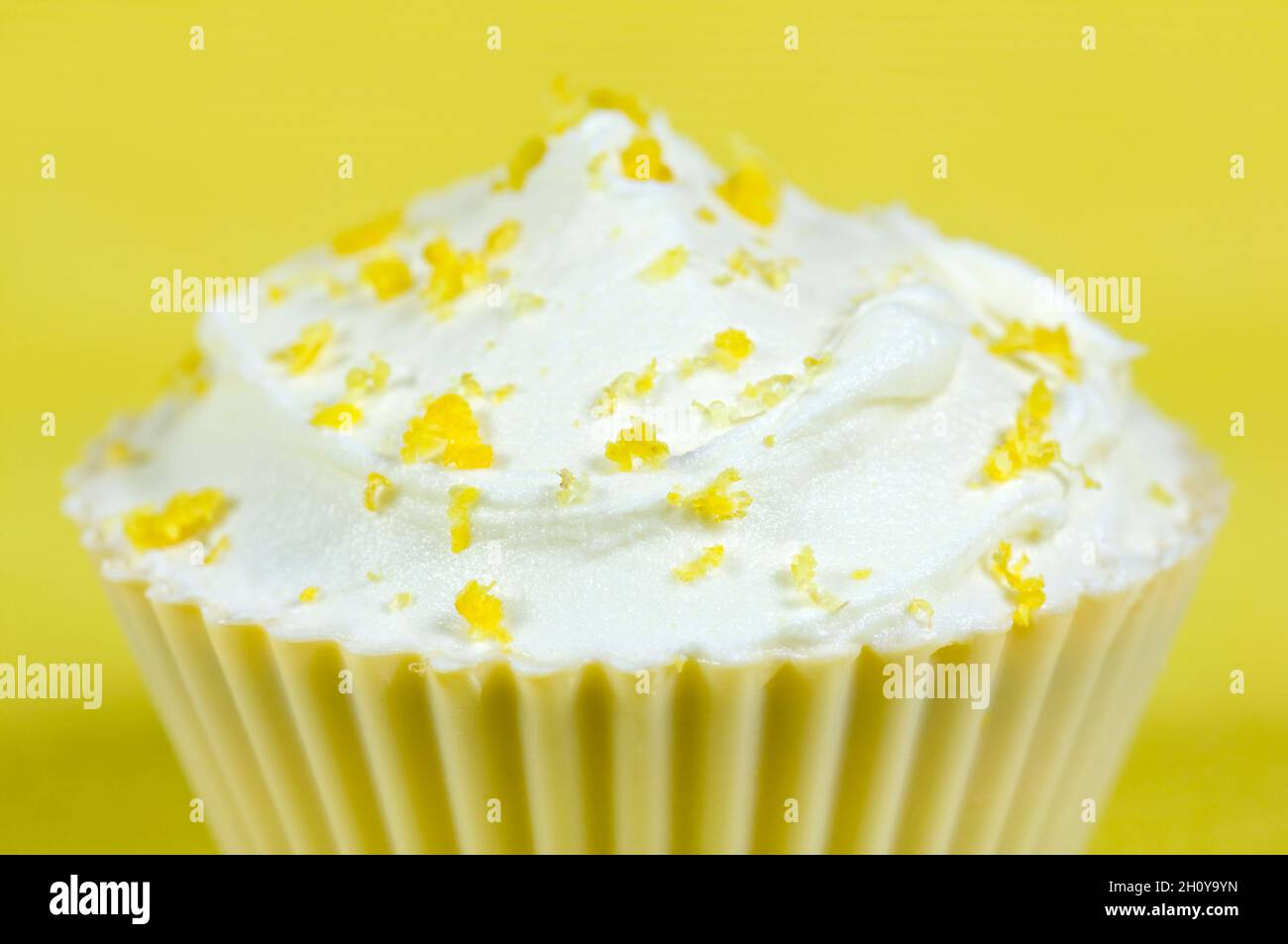 Lemon cupcake with lemon icing and sprinkled with grated lemon against a yellow background Stock Photo