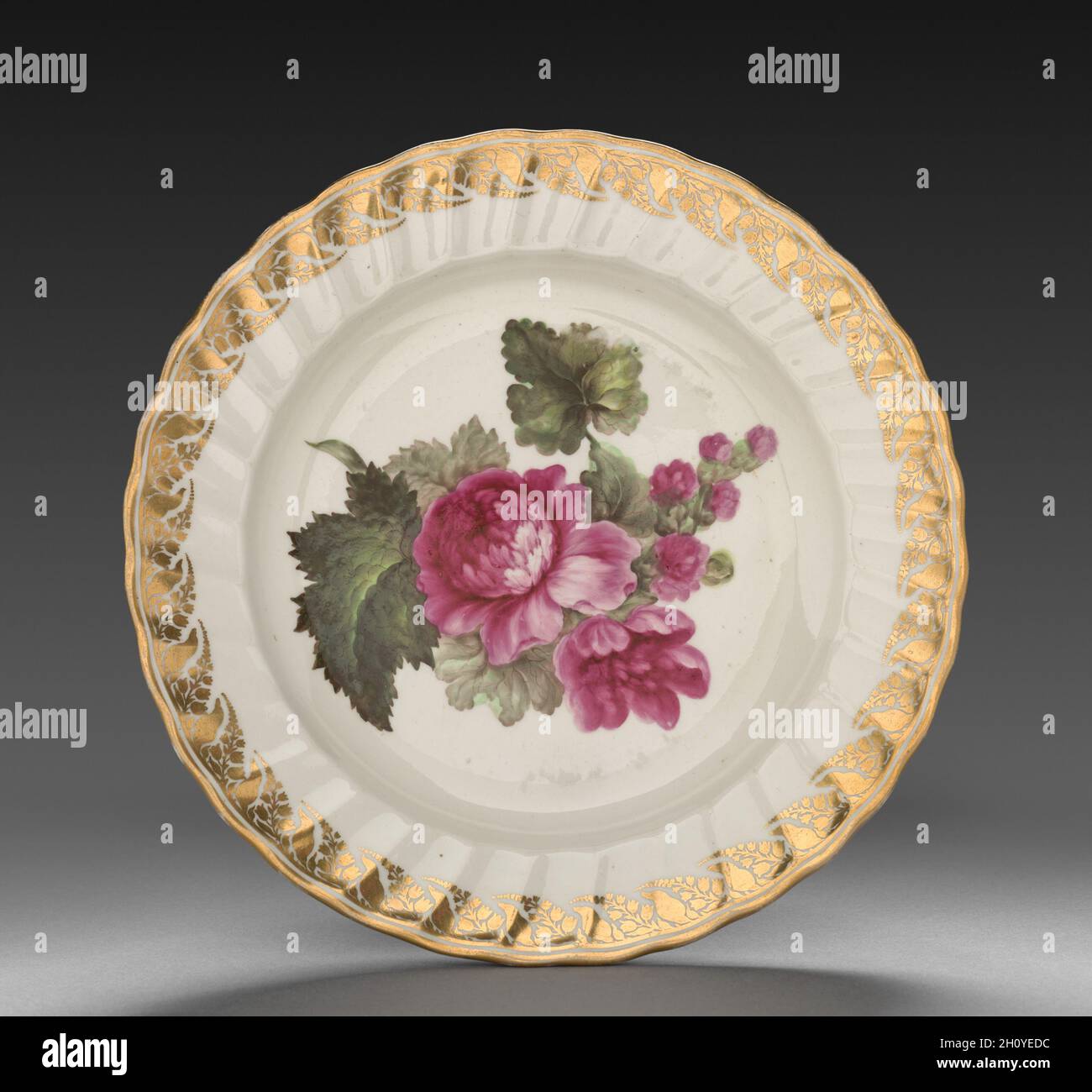 Plate from Dessert Service: Hollyhock, c. 1800. Derby (Crown Derby Period) (British). Porcelain; diameter: 23.5 cm (9 1/4 in.); overall: 3.2 cm (1 1/4 in.).  Each dish is decorated with recognizable plants, the names of which are inscribed on the base in both Latin and English. Identifying the blossoms only became customary in the late 18th century when a single piece of porcelain was decorated with one species, and flowers were represented along with leaves, stems, seed pods, and roots. All of this reflects Carolus Linnaeus’s recent invention of a scientific method to categorize all known flo Stock Photo