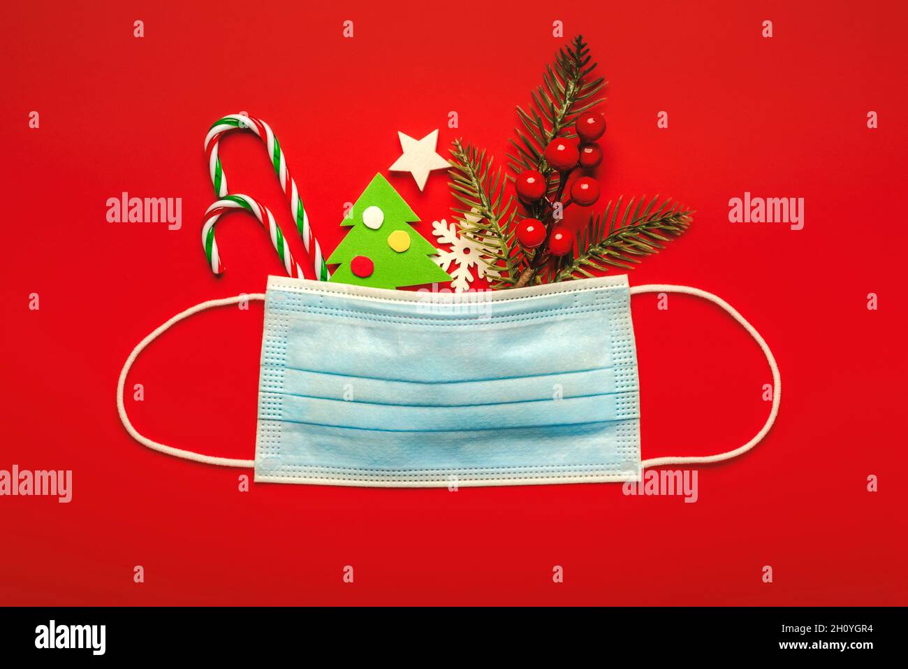 Merry Christmas. Protective surgical mask with christmas decorations over red background.Christmas concept background Stock Photo