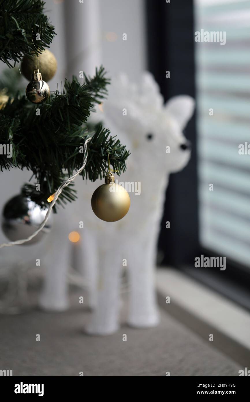 Closeup of a green Christmas tree with gold, white and silver ornaments. White deer light fixture in the background. Photographed on a balcony. Stock Photo