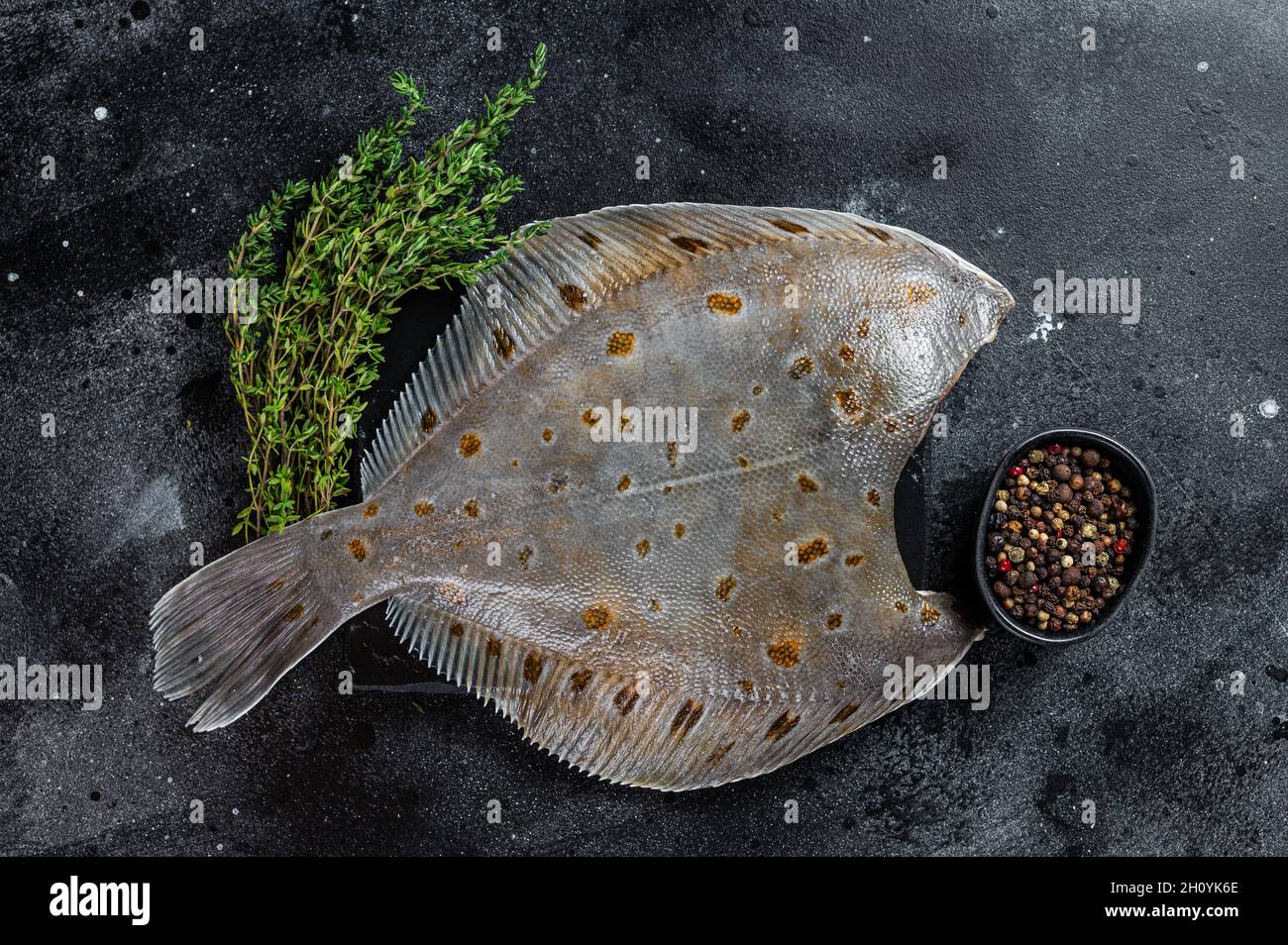 Raw flounder flatfish fish on marble board with thyme. Black background
