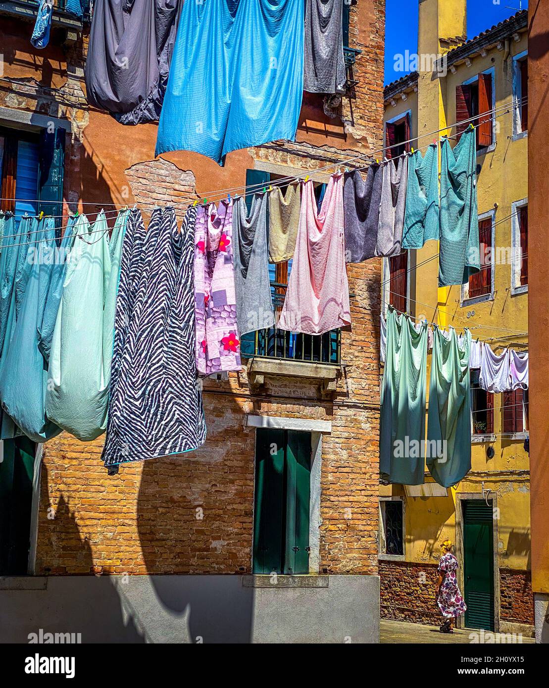 Woman walking under Hanging clothes put to dry on a small traditional street of Venice, Italy. Travel background Stock Photo